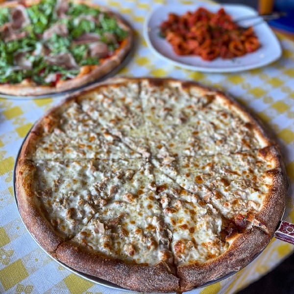 Clam pizza with melted cheese, another pizza, and a plate of pasta on a checkered tablecloth.
