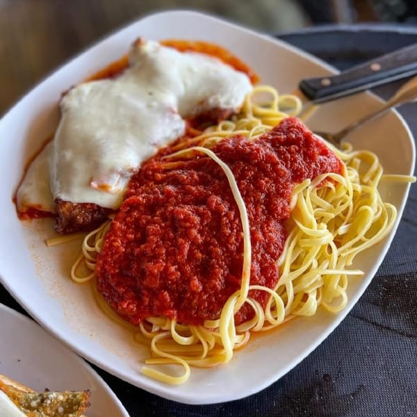 Chicken parmesan with melted mozzarella and spaghetti with red sauce on a white plate.