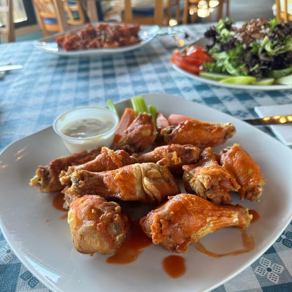 A plate of buffalo chicken wings with celery, carrots, and dipping sauce on a checkered tablecloth.