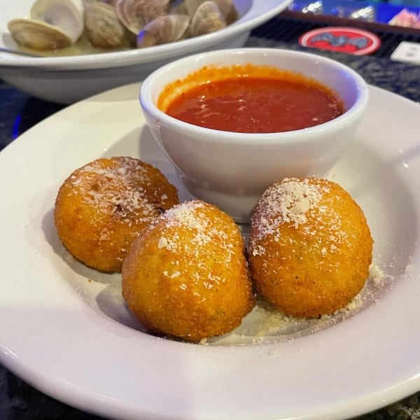 Three golden-brown fried arancini balls dusted with cheese, served with a side of red marinara sauce.