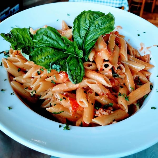 Penne pasta with red sauce, fresh basil, and parsley in a white bowl at Mangia Clam Bar.