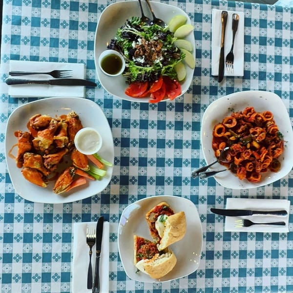 An overhead view of a blue and white checkered table set with four plates of seafood dishes.