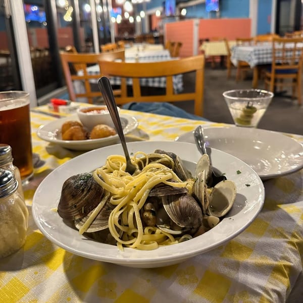 Linguine with clams, a beer, and appetizers on a yellow checkered tablecloth at Mangia Clam Bar.