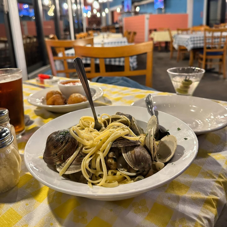 Linguine with clams, a beer, and appetizers on a yellow checkered tablecloth at Mangia Clam Bar.