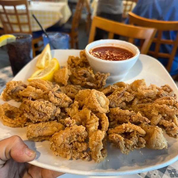 A plate of golden-brown fried calamari with lemon wedges and a side of red marinara sauce.