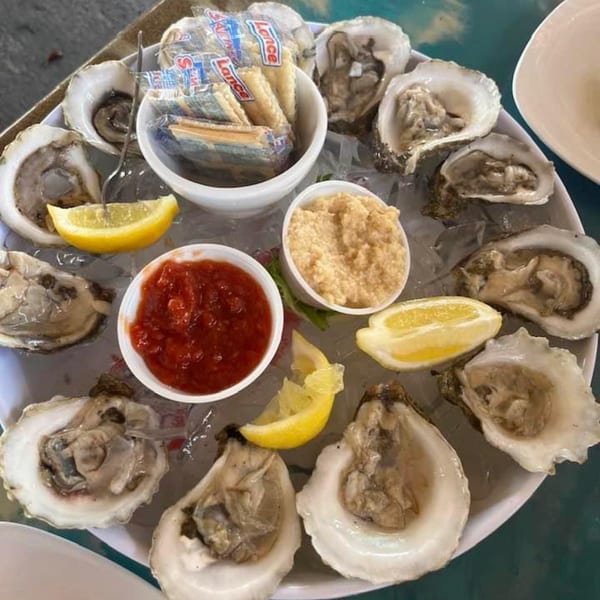 A platter of Mangia Clam Bar oysters on ice with lemon wedges, cocktail sauce, horseradish, and crackers.