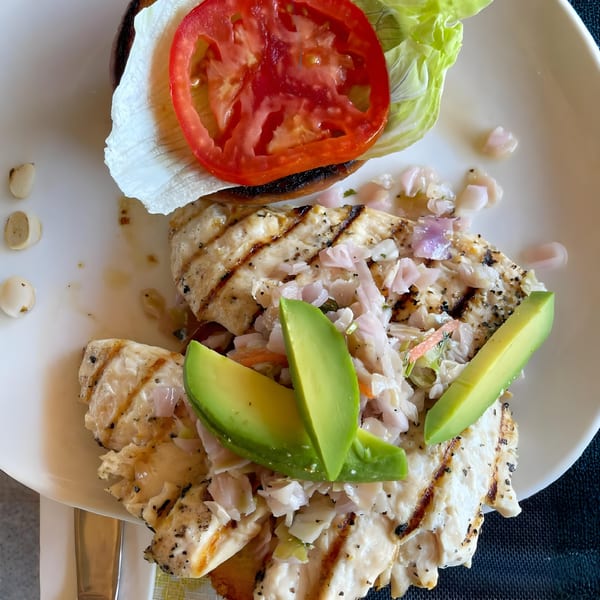Grilled fish fillets topped with avocado, salsa, and a side of lettuce and tomato.